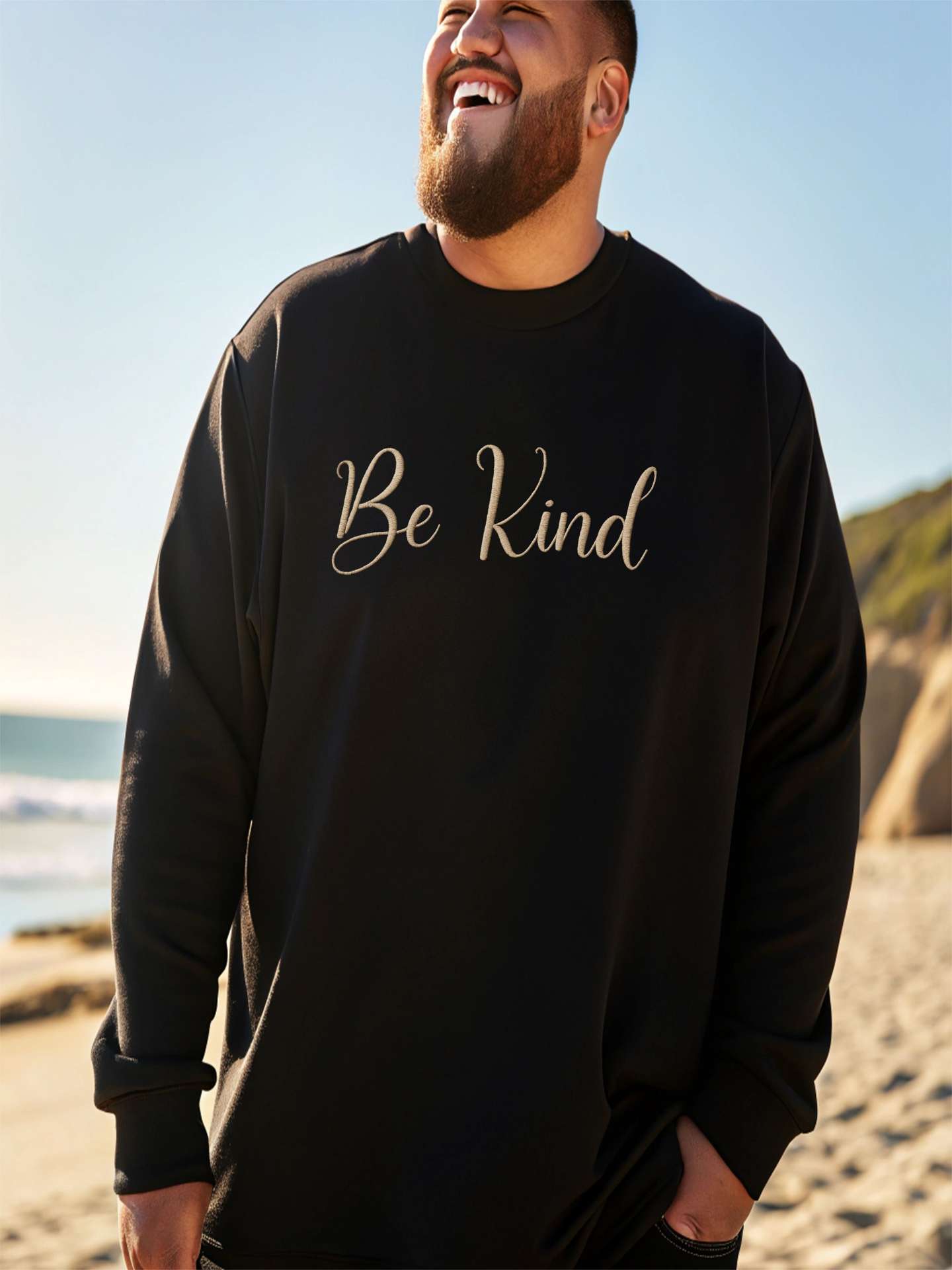 Man at the beach wearing black Embroidered Kindness Sweatshirt casual style.
