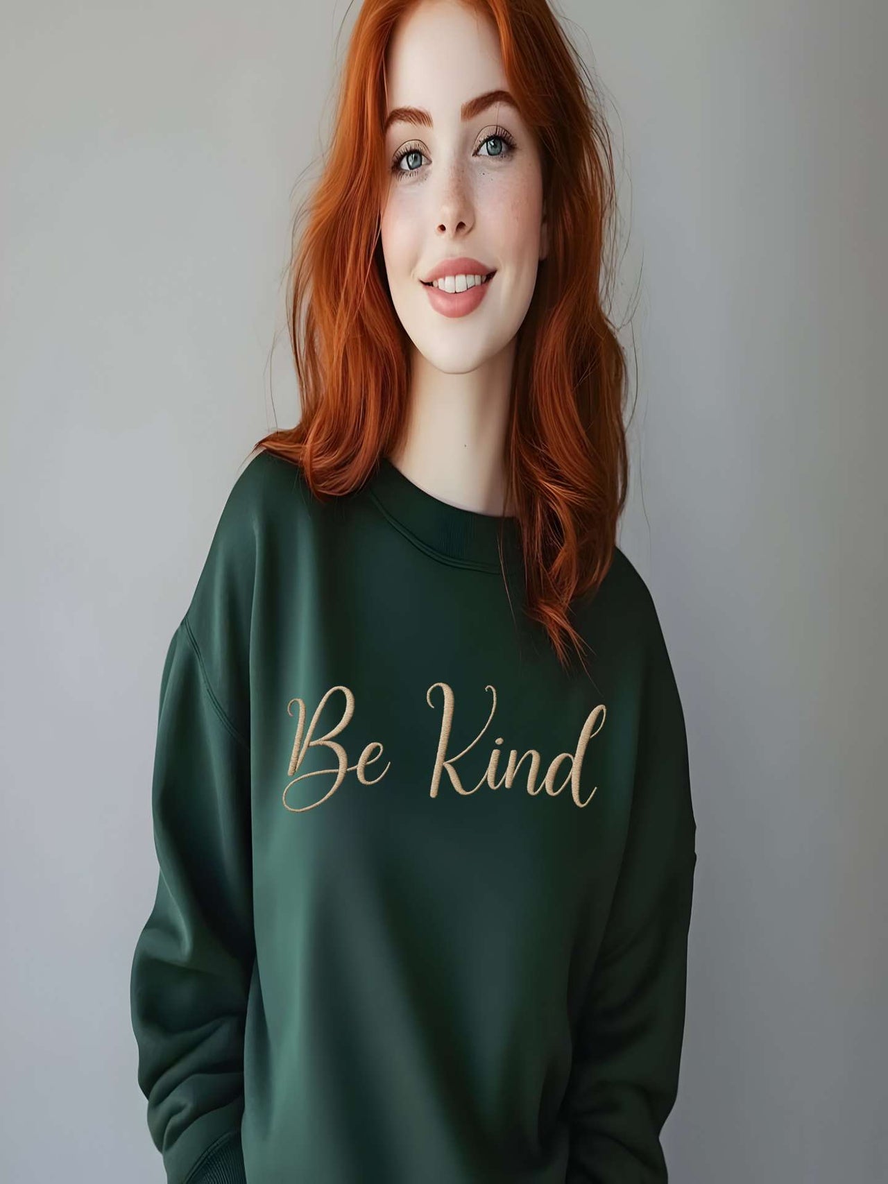 Woman wearing dark green Embroidered Kindness Sweatshirt smiling indoors.