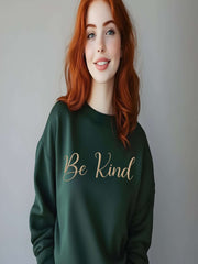 Woman wearing dark green Embroidered Kindness Sweatshirt smiling indoors.