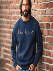 Man posing against brick wall in navy Embroidered Kindness Sweatshirt