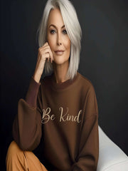 Woman sitting wearing brown Embroidered Kindness Sweatshirt indoors