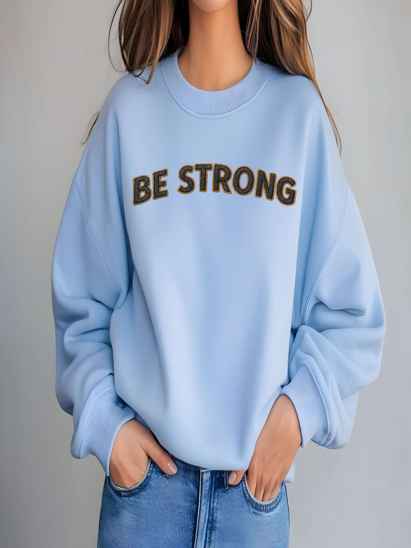 Embroidered Motivational Sweatshirt in light blue with 'BE STRONG' text design, cozy and stylish, perfect for everyday wear.