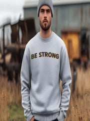 Embroidered Motivational Sweatshirt featuring the statement 'BE STRONG' on a model outdoors, showcasing casual style.