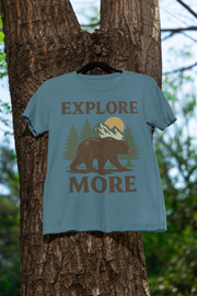 Light blue explore more t-shirt bear and mountain design, hanging on a tree in the forest. Perfect outdoor scene to showcase adventure-inspired apparel.