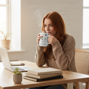 A woman enjoying a warm beverage from a Floral Ceramic Mug Bloom In Your Own Time while working at a cozy desk.