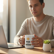 Motivational Rise and Grind Mug held by a person near a laptop, symbolizing a positive morning routine.