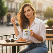 Woman holding a Coffee Is My Craft mug at an outdoor cafe, with a croissant on the table.